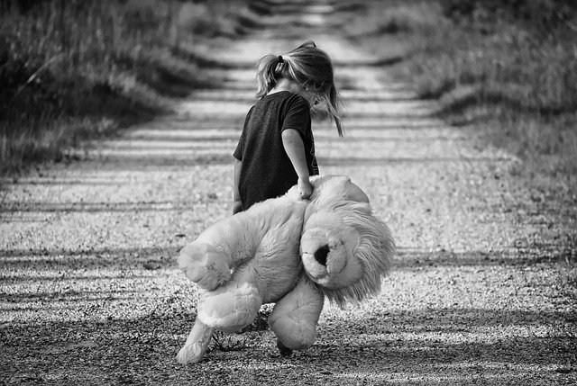 Criança carregando um ursinho com medo, triste ou deprimida. 